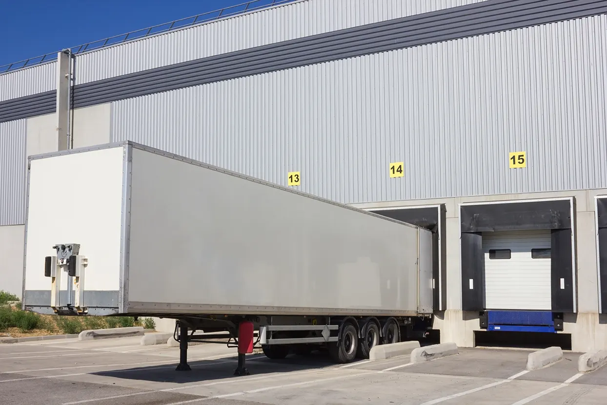 Long white trailer parked at a grey warehouse loading dock