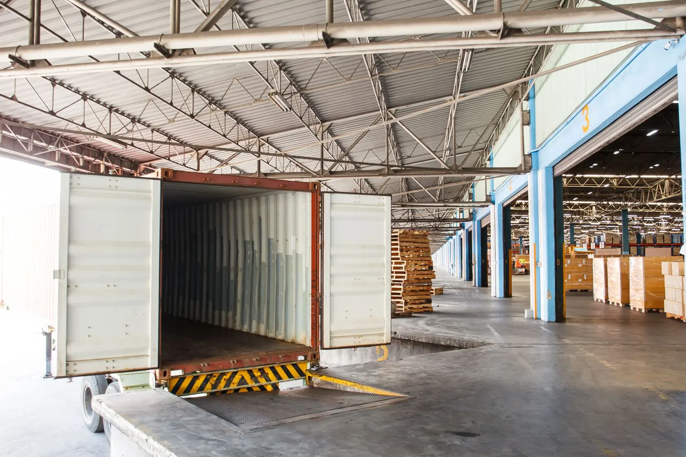 Open trailer backed up to a warehouse loading dock, ready to be loaded with pallets