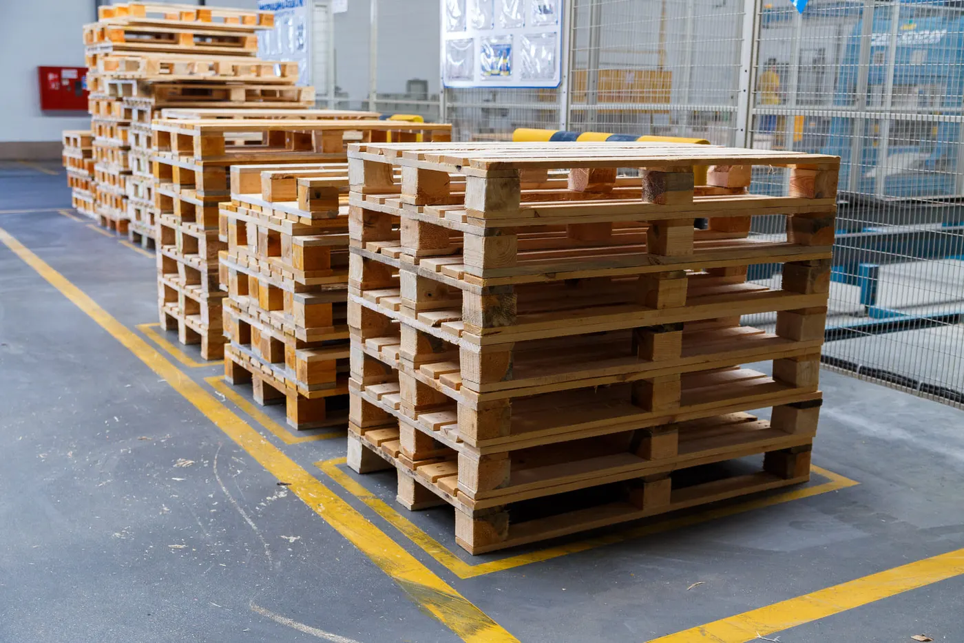 Stacks of light wood block pallets inside a warehouse, marked out by yellow floor lines