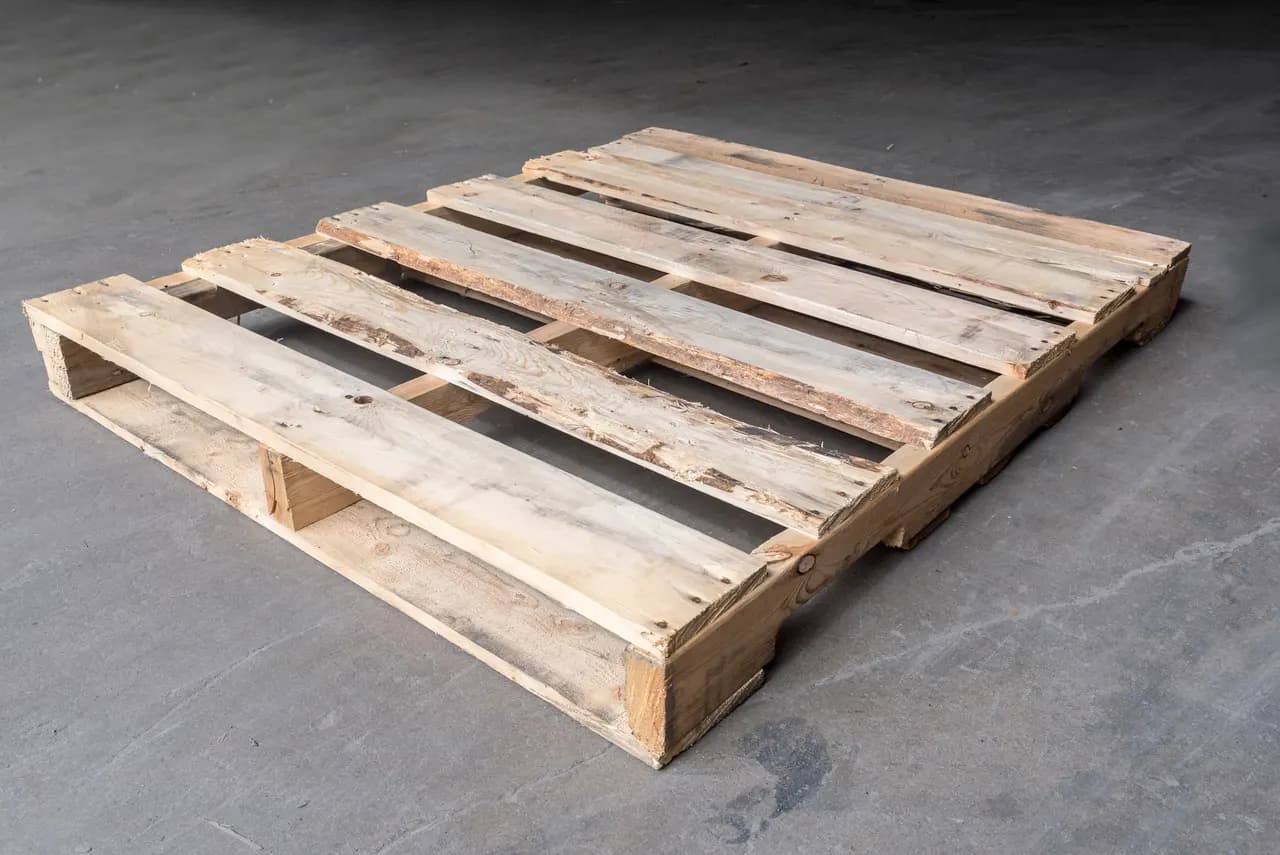 Used Grade B wood pallet with worn, weathered boards on a grey concrete floor