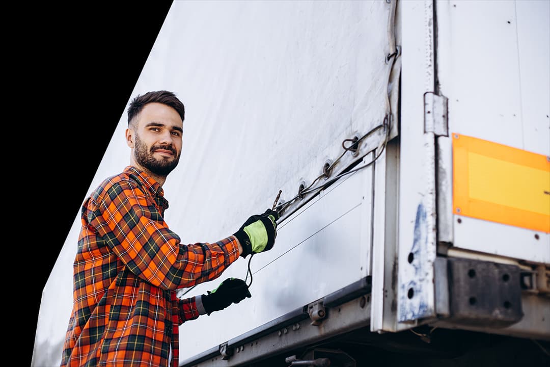 Man wearing plaid shirt tying down cover on pallet drop trailer at warehouse loading bay