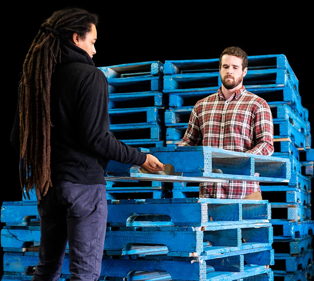 2 men lifting a 48 x 40 wood pallet onto a stack of blue colored pallets