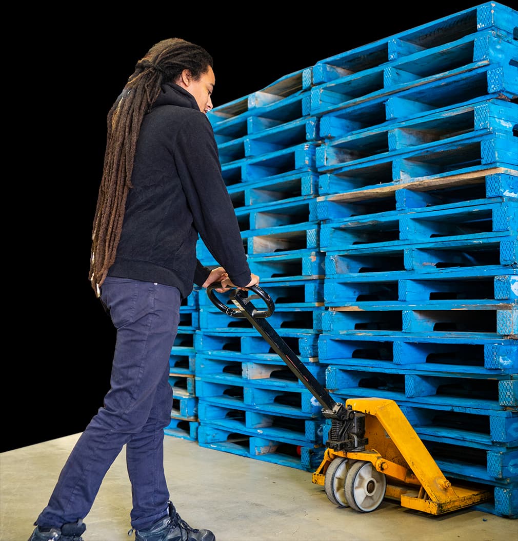 Man unloading 48 x 40 wood pallets with pallet jack in warehouse